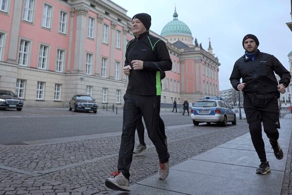 German Chancellor Olaf Scholz, left, jogs in the early morning accompanied by a bodyguard in Potsdam, Germany, Sunday, Feb. 23, 2025. (Michael Kappeler/dpa via AP)