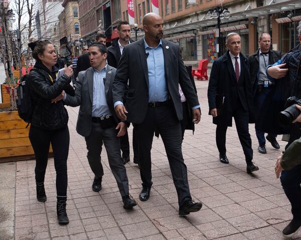 Security keeps a person from the right-wing media group Rebel News away from Prime Minister Mark Carney as he walks to a news conference, in Ottawa, Friday, May 2, 2025. (Adrian Wyld/The Canadian Press via AP)