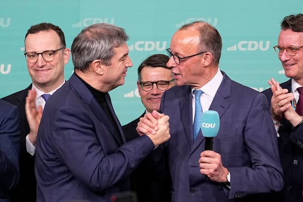 Friedrich Merz, with the microphone, the candidate of the mainstream conservative Christian Democratic Union party, shakes hands with Markus Soeder, leader of CSU and Minister-President of Bavaria, at the party headquarters in Berlin, Germany, Sunday, Feb. 23, 2025, after the German national election. (AP Photo/Martin Meissner)