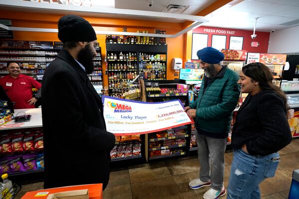 Ishar Gill, left, his father Jaspal Singh, center and his sister Jaspeet Gill right, look over the enlarged image of a check, Saturday, Dec. 28, 2024, that will be presented to the winner of $1.22 billion Mega Millions Lotto ticket that was purchased at their family's store in Cottonwood, Calif., Saturday, Dec. 28, 2024. (AP Photo/Rich Pedroncelli).