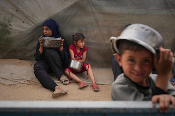 Mira Abu Shaar, 5, right, and her older sister, Raghad, 15, hold pots next to their family tent, as they wait for food to be prepared, in Muwasi, on the outskirts of Khan Younis in the southern Gaza Strip, Thursday, April 24, 2025. (AP Photo/Abdel Kareem Hana)