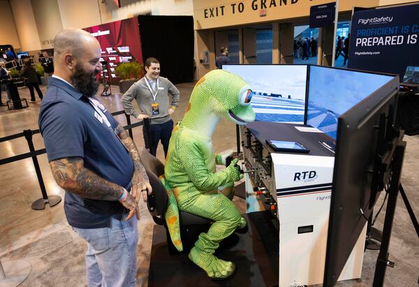 Sean DeFendi of Virginia Beach, left, watches over the GEICO Gecko as he uses the Flight Safety International flight simulator in CHI Health Center Omaha for the Berkshire Hathaway annual meeting Saturday, May 3, 2025, in Omaha, Neb. (AP Photo/Rebecca S. Gratz)