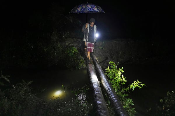 Sudirman, front, and Irfan walk on a makeshift bridge as they inspect their fish and shrimp ponds in Budong-Budong, West Sulawesi Island, Indonesia, Monday, Feb. 24, 2025. (AP Photo/Dita Alangkara)