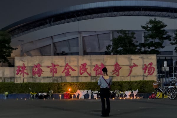 FILE - A woman stands near flowers placed outside the "Zhuhai People's Fitness Plaza", where a man deliberately rammed his car into people exercising at the sports center, killing some and injuring others in Zhuhai in southern China's Guangdong province, Nov. 12, 2024. (AP Photo/Ng Han Guan, File)