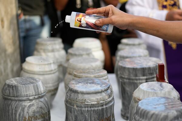 A relative sprinkles holy water on urns during an interment ceremony for victims of extrajudicial killings during the time of former President Rodrigo Duterte at the "Dambana ng Paghilom" or Shrine of Healing inside a cemetery in Caloocan City, Philippines, Wednesday, March 12, 2025. (AP Photo/Aaron Favila)