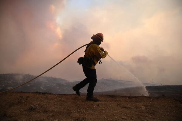 A firefighter sprays water on the ground while battling the Hughes Fire in Castaic, Calf., Wednesday, Jan. 22, 2025. (AP Photo/Ethan Swope)