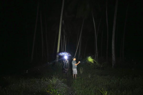 Sudirman, left, and Irfan stand among the coconut trees as they inspect their fish and shrimp ponds in Budong-Budong, West Sulawesi Island, Indonesia, Monday, Feb. 24, 2025. (AP Photo/Dita Alangkara)