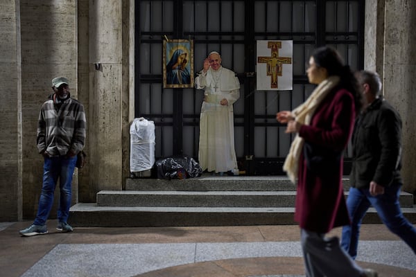 People walk past a cardboard with the image of Pope Francis near St. Peter's Square in Rome, Saturday, March 8, 2025. (AP Photo/Francisco Seco)