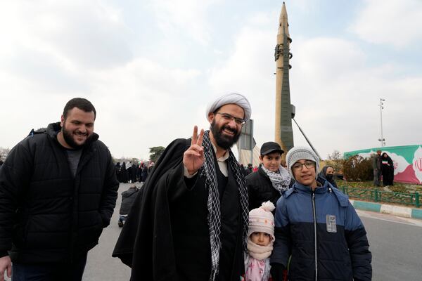 A cleric flashes a victory sign near a domestically-built missile during a rally commemorating anniversary of Iran's 1979 Islamic Revolution that toppled the late pro-U.S. Shah Mohammad Reza Pahlavi and brought Islamic clerics to power, in Tehran, Iran, Monday, Feb. 10, 2025. (AP Photo/Vahid Salemi)