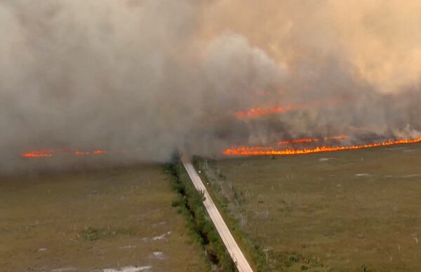 In this image taken from video provided by WSVN-TV, a brush fire burns across and over Card Sound Road, the only other road connecting the Keys to Florida City on the mainland, as it remains closed Tuesday, March 18, 2025, south of Dade County, Fla. (WSVN-TV via AP)