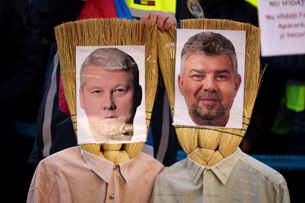 FILE - A Romanian policeman holds effigies made of brooms of Prime Minister Marcel Ciolacu, right, and Interior Minister Catalin Predoiu, left, during a protest in Bucharest, Romania, Jan. 17, 2025. (AP Photo/Vadim Ghirda, File)