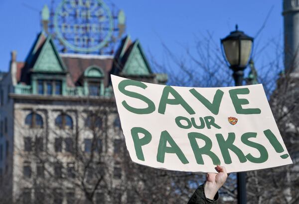 A protester raises a sign that reads "Save Our Parks" under the Scranton Electric City building at a "Save Steamtown" rally to protest the Trump administration layoffs at the Steamtown National Historic Site in Scranton, Pa., Saturday, Feb. 22, 2025. (Aimee Dilger/WVIA via AP)