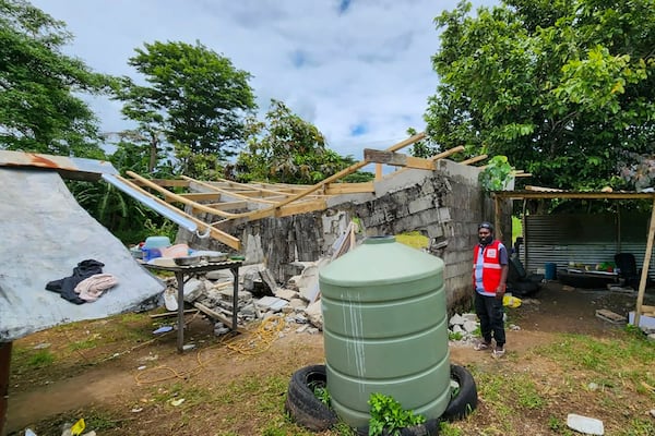 In this photo released by Vanuatu Red Cross Society, a Red Cross volunteer stands beside a damaged house in Efate, Vanuatu, Thursday, Dec. 19, 2024, following a powerful earthquake that struck just off the coast of Vanuatu in the South Pacific Ocean. (Vanuatu Red Cross Society via AP)