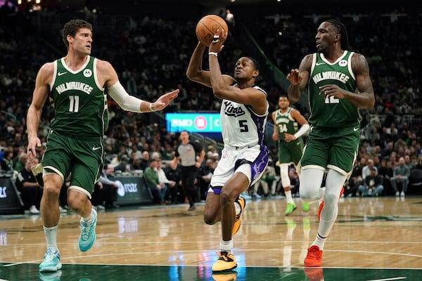 Sacramento Kings' De'Aaron Fox (5) drives to the basket between Milwaukee Bucks' Brook Lopez (11) and Taurean Prince during the first half of an NBA basketball game, Tuesday, Jan. 14, 2025, in Milwaukee. (AP Photo/Aaron Gash)