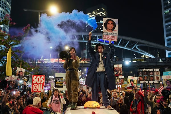 Demonstrators hold signs and flares during a protest calling for the immediate release of the hostages held in the Gaza Strip by the Hamas militant group in Tel Aviv, Israel, on Monday, Jan. 13, 2025. (AP Photo/Ohad Zwigenberg)