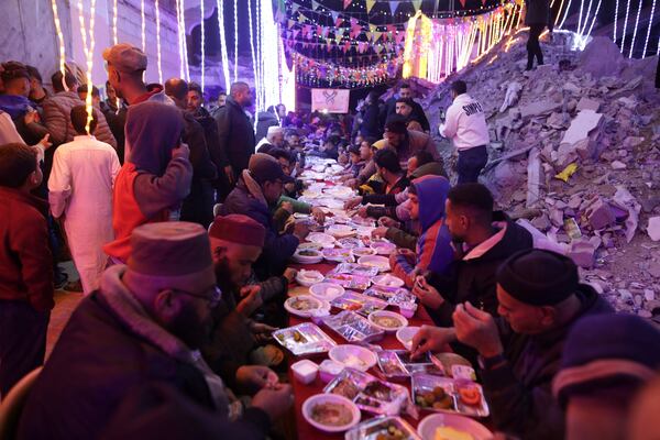 Palestinians hold a collective suhoor meal next to their destroyed homes for the holy month of Ramadan in Khan Younis, southern Gaza Strip, Friday, Feb. 28, 2025. Arabic reads: "Ramadan." (AP Photo/Jehad Alshrafi)