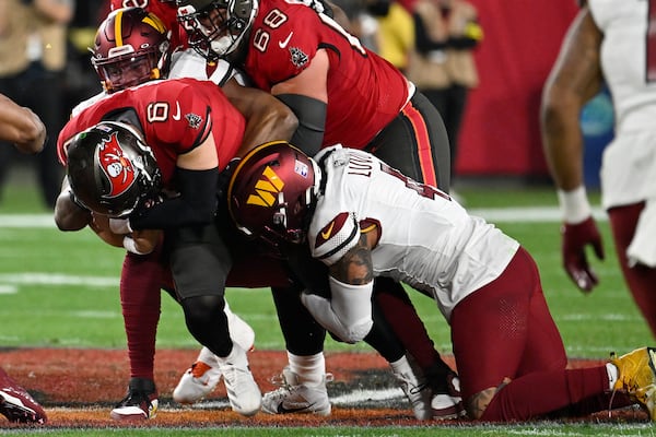 Tampa Bay Buccaneers quarterback Baker Mayfield (6) is tackled by Washington Commanders linebacker Frankie Luvu, right, and defensive end Dorance Armstrong during the first half of an NFL wild-card playoff football game in Tampa, Fla., Sunday, Jan. 12, 2025. (AP Photo/Jason Behnken)