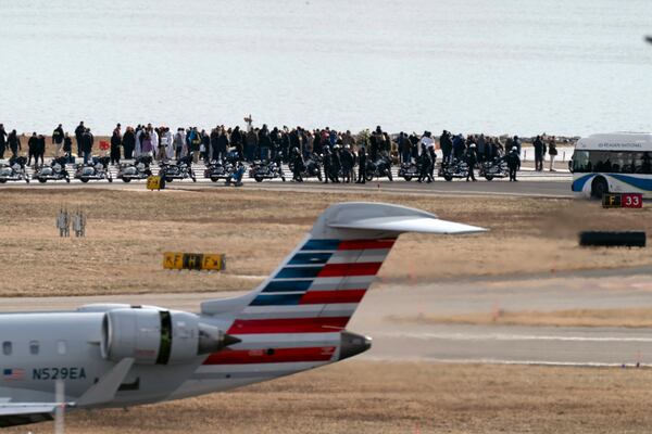 An American Airlines jet passes as family members of the victims of a mid-air collision between an American Airlines jet and an Army helicopter stand at the end of runway 33 near the wreckage site in the Potomac River at Ronald Reagan Washington National Airport, Sunday, Feb. 2, 2025, in Arlington, Va. (AP Photo/Jose Luis Magana)