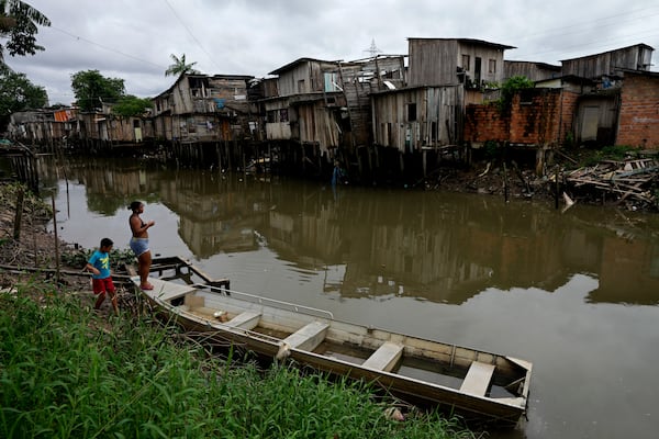 FILE - A mother and son walk on the bank of the Tucunduba Channel where stilt homes stand in the Terra Firme neighborhood of Belem, Brazil, March 26, 2024. (AP Photo/Eraldo Peres, File)