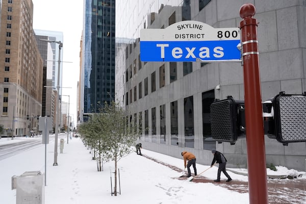 People shovel snow off the sidewalk Tuesday, Jan. 21, 2025, in downtown Houston. (AP Photo/Ashley Landis)