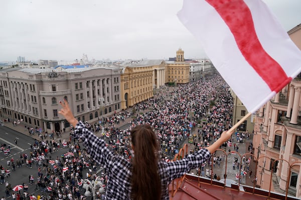 FILE - A woman waves an old Belarusian national flag from a roof as opposition supporters march to Independence Square in Minsk, Belarus, on Aug. 23, 2020. (AP Photo/Evgeniy Maloletka, File)