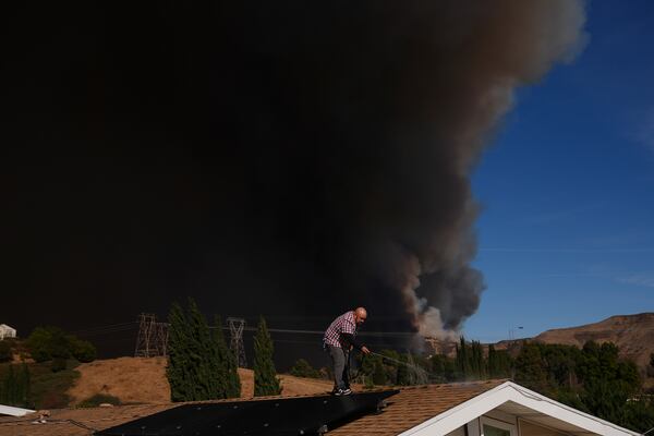 A home owner sprays water from the top of the roof at his brother's home Castaic, Calif., as a large plume of smoke caused by the Hughes Fire rises from Castaic Lake Wednesday, Jan. 22, 2025. (AP Photo/Marcio Jose Sanchez)