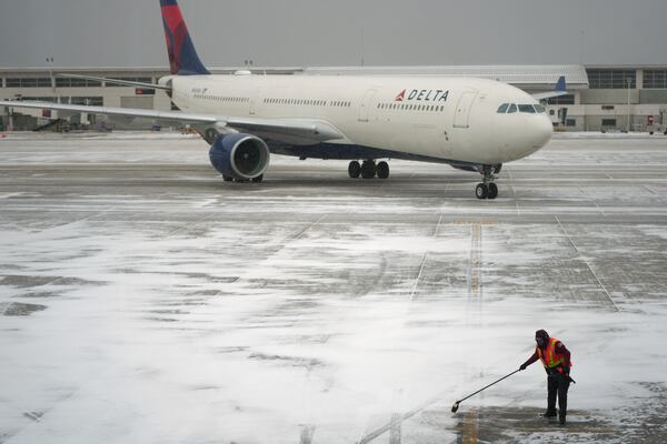 A worker clears snow from an apron before guiding a Delta Air Lines jet at the Detroit Metropolitan Wayne County Airport in Romulus, Mich., Monday, Jan. 6, 2025. (AP Photo/Charlie Riedel)