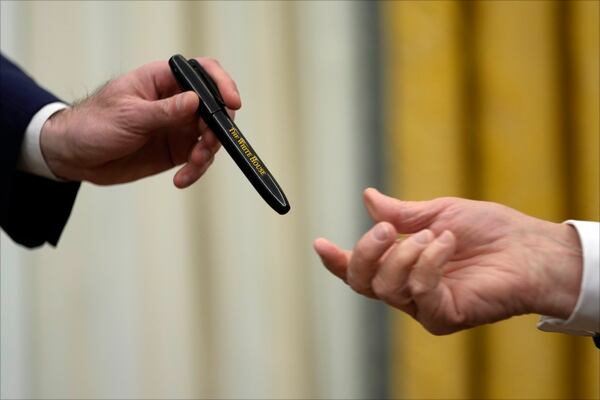 President Donald Trump hands a pen to White House staff secretary Will Scharf as he signs executive orders in the Oval Office of the White House, Thursday, Jan. 23, 2025, in Washington. (AP Photo/Ben Curtis)