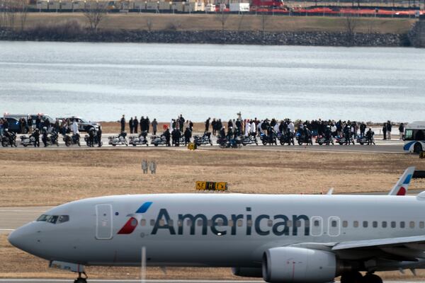 An American Airlines jet passes as families of the victims of a mid-air collision between an American Airlines jet and an Army helicopter stand near the wreckage site in the Potomac River at the end of the runway 33 from Ronald Reagan Washington National Airport, Sunday, Feb. 2, 2025, in Arlington, Va. (AP Photo/Jose Luis Magana)