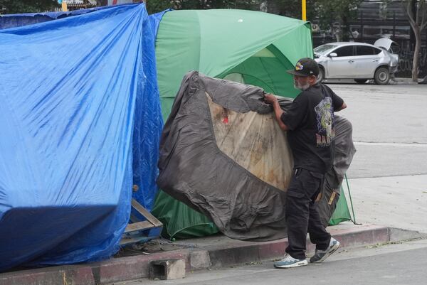 A man carries a mattress into a tent set up on a sidewalk, Monday, May 12, 2025, in Los Angeles. (AP Photo/Damian Dovarganes)