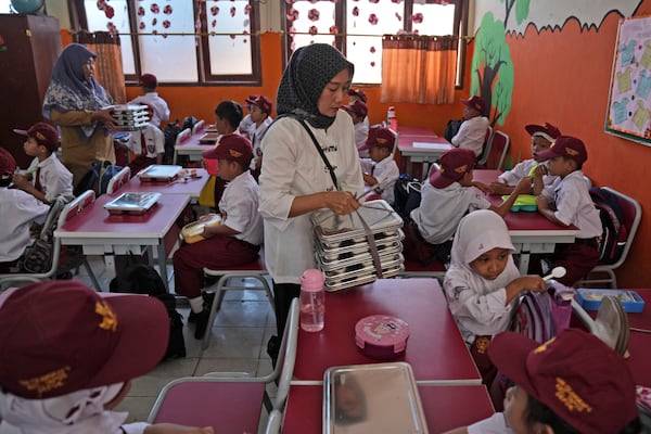 Members of school committee distribute meals to students during the kick off of President Prabowo Subianto's ambitious free meal program to feed children and pregnant women nationwide despite critics saying that its required logistics could hurt Indonesia's state finances and economy, at an elementary school in Depok, West Java, Indonesia, Monday, Jan. 6, 2025. (AP Photo/Dita Alangkara)