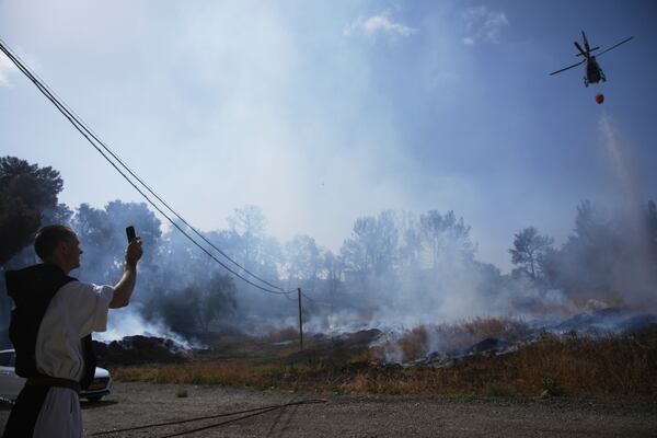A Roman Catholic Trappist monk films an Israeli fire crew helicopter battling a wildfire outside his monastery in Latrun, Israel, outside of Jerusalem, Thursday, May 1, 2025. (AP Photo/Ohad Zwigenberg)