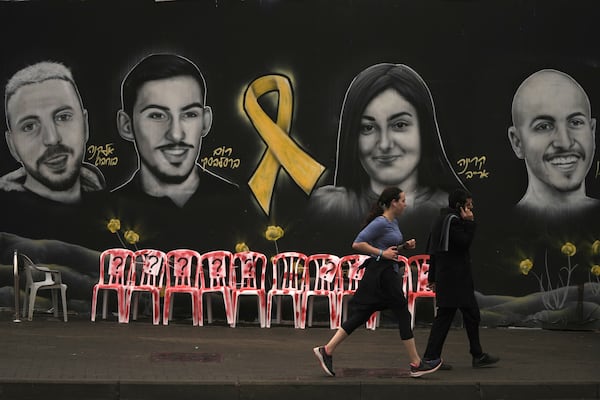 People walk and jog past an installation and a mural of portraits of hostages held by Hamas in the Gaza Strip, in Jerusalem, Friday, Jan. 24, 2025. (AP Photo/Mahmoud Illean)