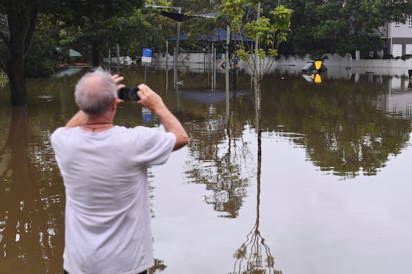 A resident takes photos of a flooded road, in Oxley, in Brisbane, Australia, Monday, March 10, 2025. (Jono Searle/AAP Image via AP)