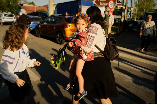 A woman carries a baby as she walks ahead of a media scrum around Calin Georgescu, winner of the first round of last year's annulled election, and Presidential candidate George Simion during in the first round of the presidential election redo in Mogosoaia, Romania, Sunday, May 4, 2025. (AP Photo/Vadim Ghirda)