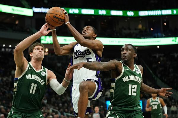 Sacramento Kings' De'Aaron Fox, middle, drives to the basket between Milwaukee Bucks' Brook Lopez (11) and Taurean Prince (12) during the first half of an NBA basketball game Tuesday, Jan. 14, 2025, in Milwaukee. (AP Photo/Aaron Gash)