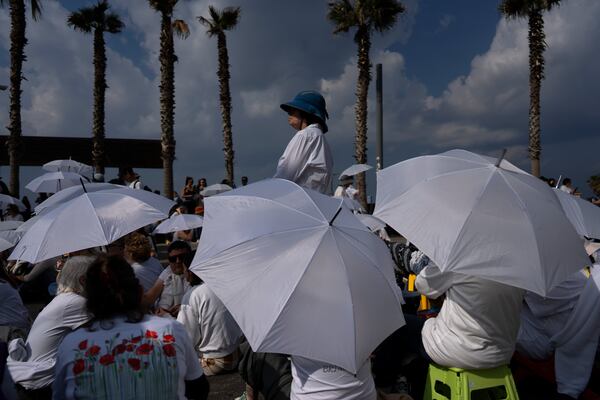 Activists sit on a road with white umbrellas during a protest calling for the release of hostages held in the Gaza Strip, in front of the U.S. Embassy branch office in Tel Aviv, Israel, Friday, Jan. 31, 2025. (AP Photo/Oded Balilty)