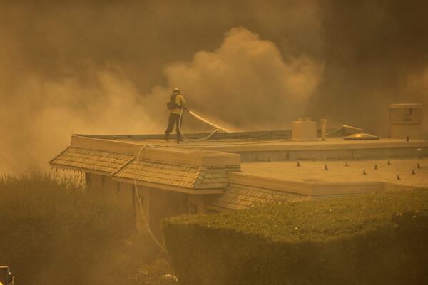 A firefighter tries to contain the Palisades Fire from a rooftop in the Pacific Palisades neighborhood of Los Angeles, Tuesday, Jan. 7, 2025. (AP Photo/Ethan Swope)