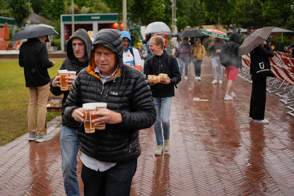 FILE - Tennis fans, some holding beers, shield themselves from the rain during third round matches of the French Open tennis tournament at the Roland Garros stadium in Paris, Friday, May 31, 2024. (AP Photo/Thibault Camus, File)