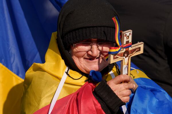 A woman drapped in the Romanian flag holds a cross during a protest by supporters of Calin Georgescu, the winner of Romania's first round of presidential election which the Constitutional Court later annulled in Bucharest, Romania, Monday, Feb. 10, 2025. (AP Photo/Vadim Ghirda)