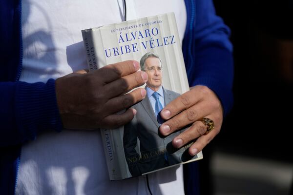 A supporter of Colombia's former President Alvaro Uribe holds a book about him outside the court where he is attending a hearing on charges of witness tampering and bribery in Bogota, Colombia, Monday, Feb. 10, 2025. (AP Photo/Fernando Vergara)