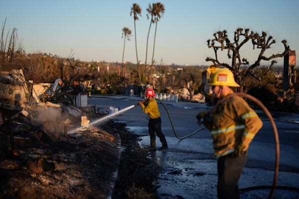 Apple Valley Fire District Captain Manuel Lafarga, center, and firefighter James Lyons hose down hotspots in the aftermath of the Palisades Fire in the Pacific Palisades neighborhood of Los Angeles, Monday, Jan. 13, 2025. (AP Photo/John Locher)