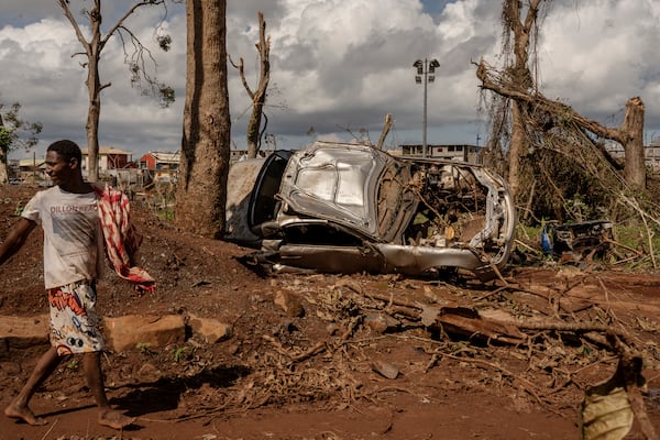 A man walks by a destroyed car in Mirereni, Mayotte, Friday, Dec. 20, 2024. (AP Photo/Adrienne Surprenant)