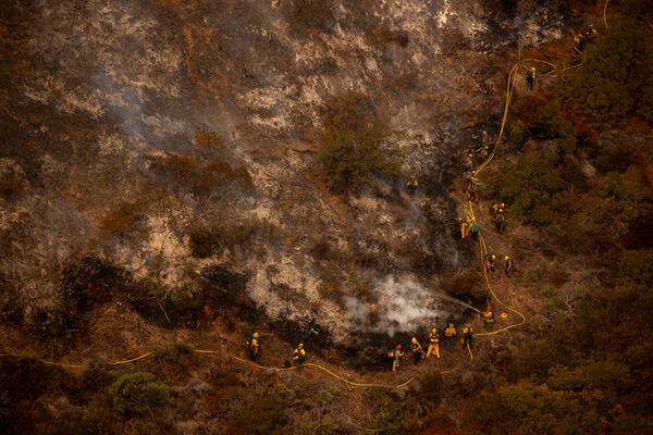 A group of firefighters traverse a steep hill while battling the Palisades Fire in the Mandeville Canyon neighborhood of Los Angeles, Calif., Saturday, Jan. 11, 2025. (Stephen Lam/San Francisco Chronicle via AP)