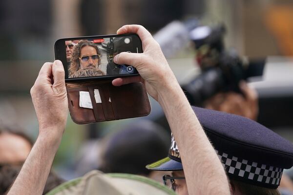 A person takes a smart phone picture as Russell Brand arrives at Westminster Magistrates' court in London, Friday, May 2, 2025, where he faces, rape and sexual assault charges involving four women. (AP Photo/Alberto Pezzali)