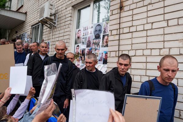Ukrainian soldiers walk though human corridor with people holding photos of their missed relatives after returning from captivity after a POWs exchange between Russia and Ukraine, in Chernyhiv region, Ukraine, Saturday, May 24, 2025. (AP Photo/Evgeniy Maloletka)