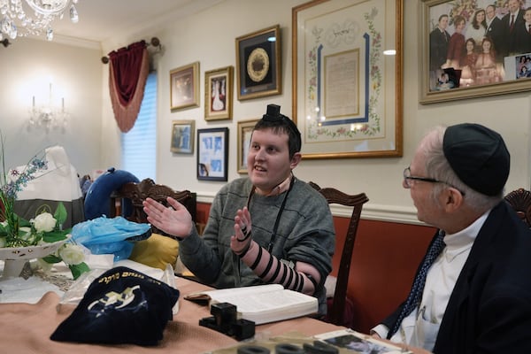 Dov Marcus, left, sings with his mother, Debbie Marcus, after wrapping the leather straps of tefillin and praying with his uncle, Chaim Orlan, right, in Teaneck, N.J., on Friday, Dec. 20, 2024. (AP Photo/Luis Andres Henao)