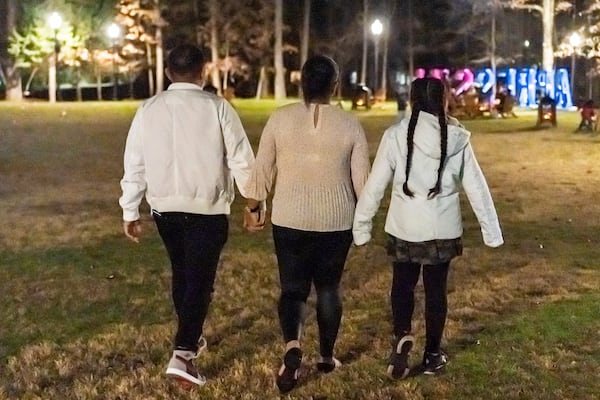 A mother and daughter, humanitarian parole beneficiaries from Venezuela sponsored by Sandra McAnany, and the husband/father they were able to reunite enjoying walking around the Christmas lights, Dec. 17, 2023, in an Atlanta, Ga., suburb. (Sandra McAnany via AP)