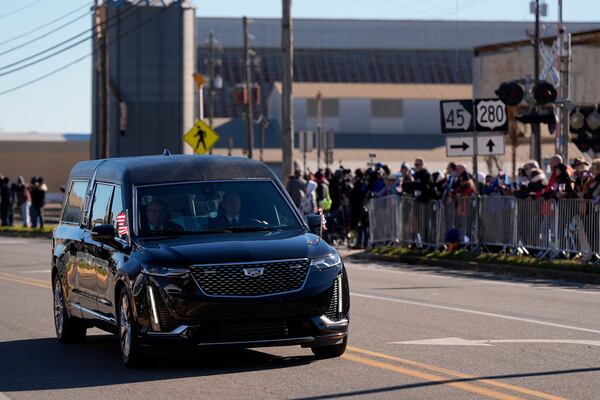 People watch as a hearse carrying the flag-draped casket of former President Jimmy Carter passes a grain elevator as it moves through downtown Plains, Ga., Saturday, Jan. 4, 2025. (AP Photo/Mike Stewart)