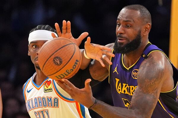 Oklahoma City Thunder guard Shai Gilgeous-Alexander, left, and Los Angeles Lakers forward LeBron James reach for a loose ball during the second half of an Emirates NBA Cup basketball game, Friday, Nov. 29, 2024, in Los Angeles. (AP Photo/Mark J. Terrill)